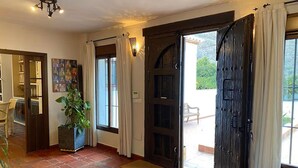 Una habitació àmplia amb terra de rajola, un gran finestral amb cortines, una porta que dona a l'exterior i una planta en test.