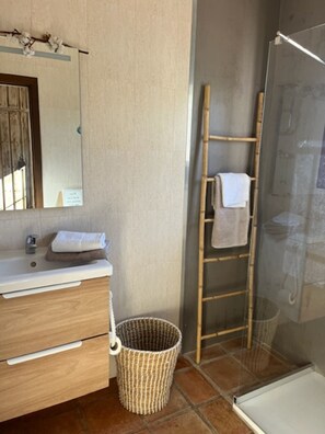 Un baño con tocador de madera, espejo, toallero, zona de ducha y una cesta tejida.