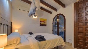 Une chambre à coucher comprenant un lit, une lampe de chevet, un appareil de climatisation et une porte avec un panneau en verre.