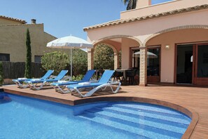 A swimming pool with lounge chairs and umbrellas, a patio area, and a building with a tiled roof.