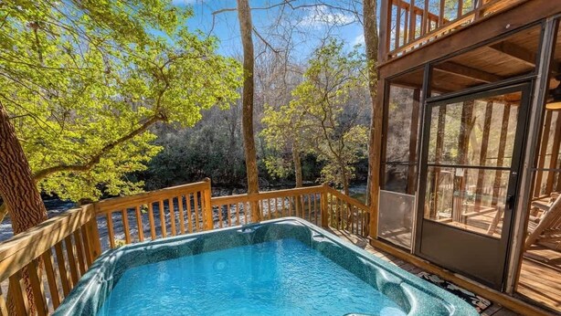 A hot tub on a wooden deck with a view of trees and a glass door leading to an interior space. - Talking Waters - Fishing Camp (Blue Ridge)