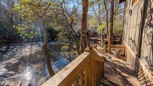 A wooden deck overlooking a river with trees and a building in the background. - Talking Waters - Fishing Camp (Blue Ridge)