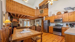 A spacious kitchen with wooden cabinets, a central island, and a dining area with wooden chairs. - Talking Waters - Fishing Camp (Blue Ridge)