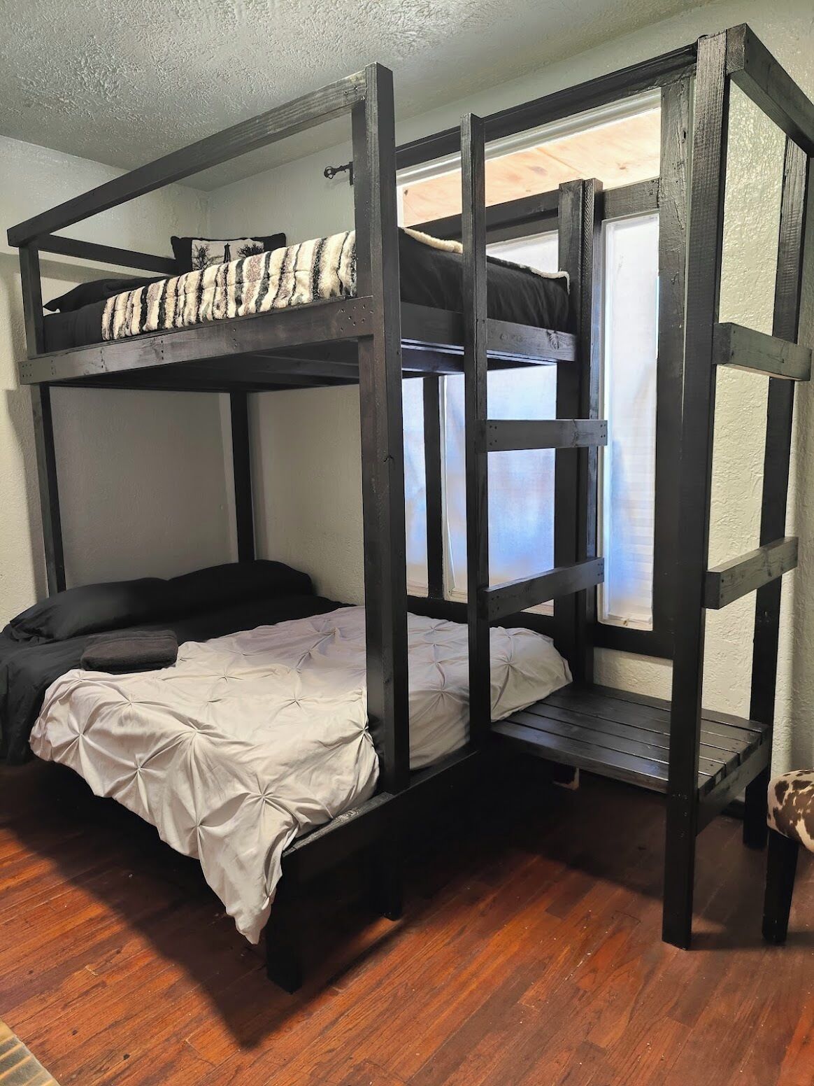 Una litera con ventana, suelo de madera y una alfombra pequeña.