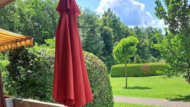 Un patio con un paraguas rojo, una mesa de madera y vistas a un jardín cuidado.