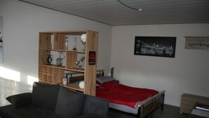 Una habitación con una cama, una estantería de madera, un sofá y un cuadro en la pared.