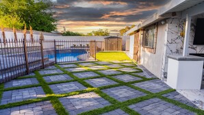 A backyard with a swimming pool, a fenced area, and a paved patio with grass edging. - Beautiful and cozy family house with pool and barbecue. (Las Vegas)