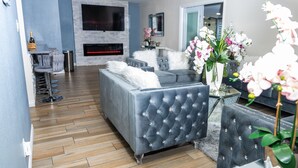 A modern living room with a grey sofa, a fireplace, and a TV mounted on the wall. - Beautiful and cozy family house with pool and barbecue. (Las Vegas)