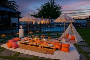 An outdoor dining setup with a pool, umbrellas, and a teepee.