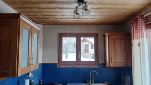Una cocina con armarios de madera, encimera azul, ventana con vista a una casa y una lámpara colgante.