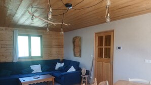 Un salón acogedor con un sofá azul, una mesa de centro de madera y una mesa de comedor con sillas. Hay una puerta de madera y una ventana con cortinas.