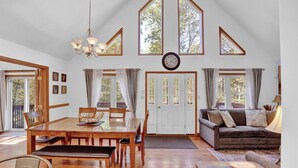 Amplia sala de estar con una mesa de comedor de madera, un sofá y ventanas grandes.