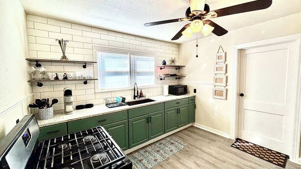 A kitchen with green cabinets, a black stove, a ceiling fan, and a window with blinds.