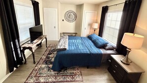 A bedroom with a bed, a TV, a desk, a lamp, and a patterned rug.