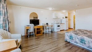 A compact hotel room with a bed, a desk with a computer, a small kitchenette, and a bathroom. - Western Budget Plus Cold Lake (Cold Lake)