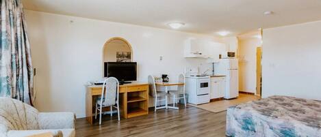 A compact hotel room with a bed, a desk with a computer, a small kitchenette, and a bathroom.