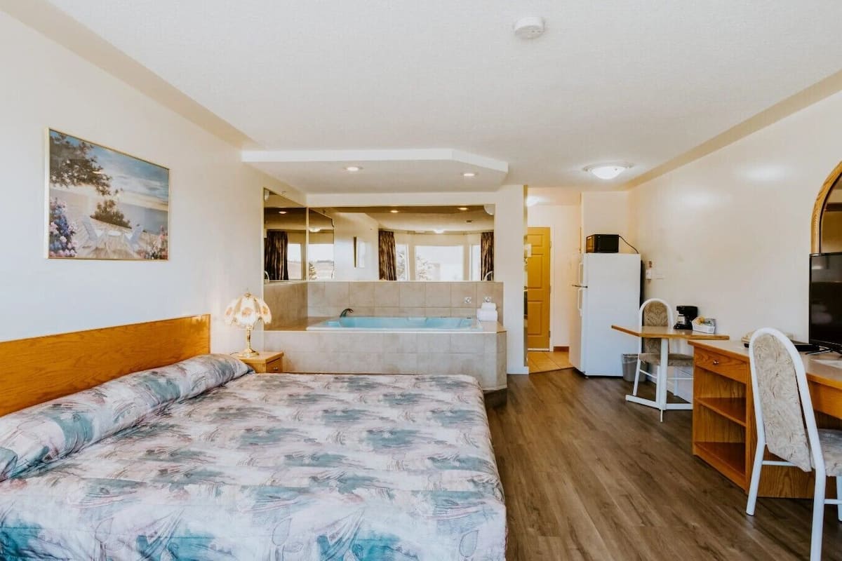 A bedroom with a bed, a desk, a chair, a sink, and a bathtub.