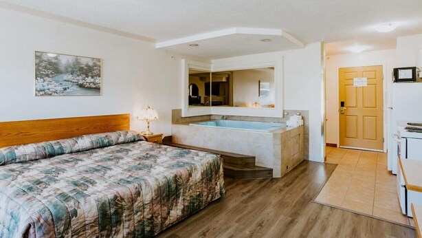 A bedroom with a bed, a nightstand, a bathroom with a sink and mirror, and a door. - Western Budget Plus Cold Lake (Cold Lake)