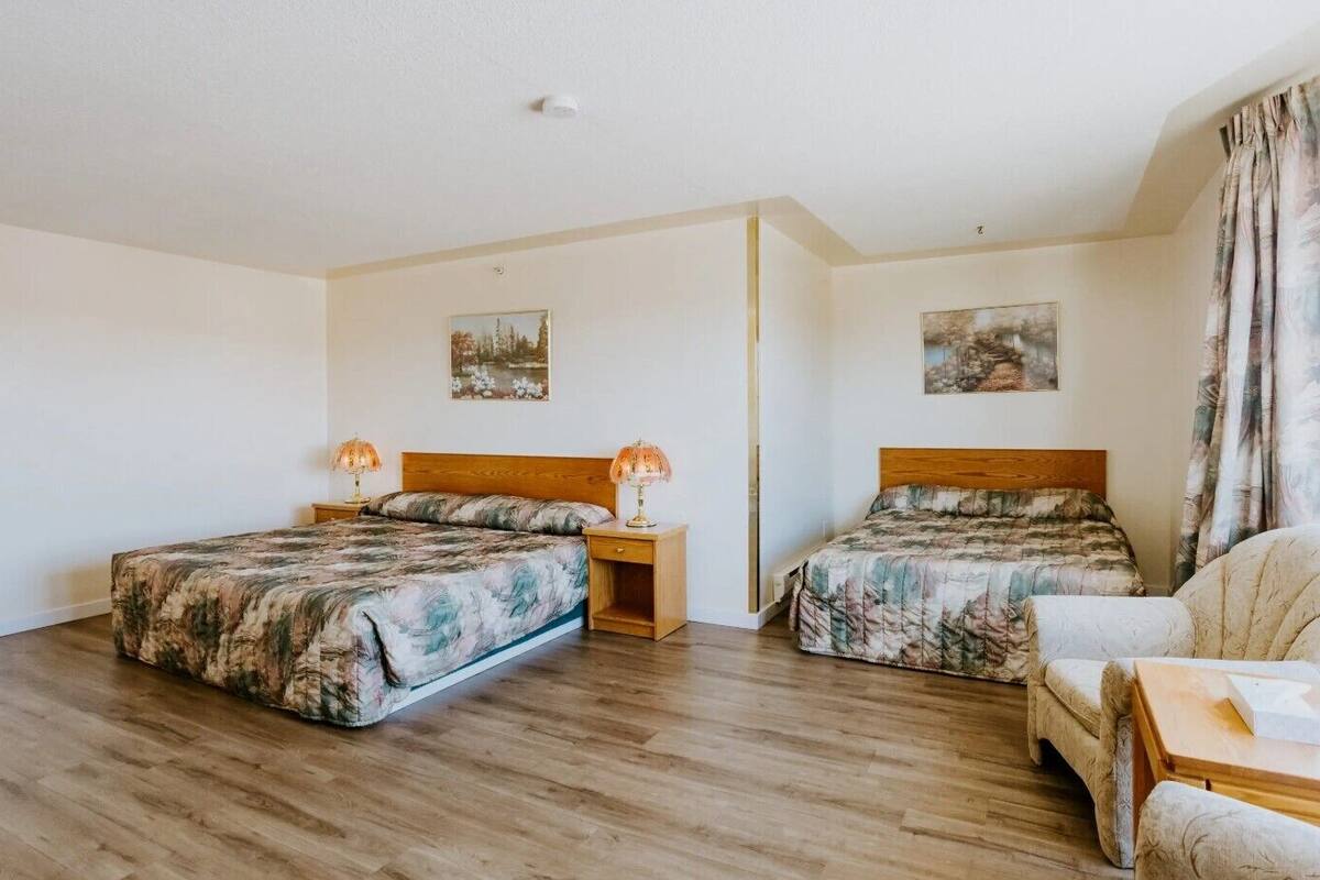 A hotel room with two beds, wooden headboards, and a small sofa.