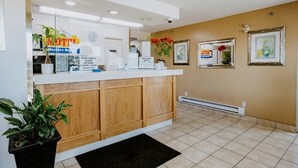 A reception area with a closed front desk, a clock, a sign indicating closed hours, and a potted plant. - Western Budget Plus Cold Lake (Cold Lake)