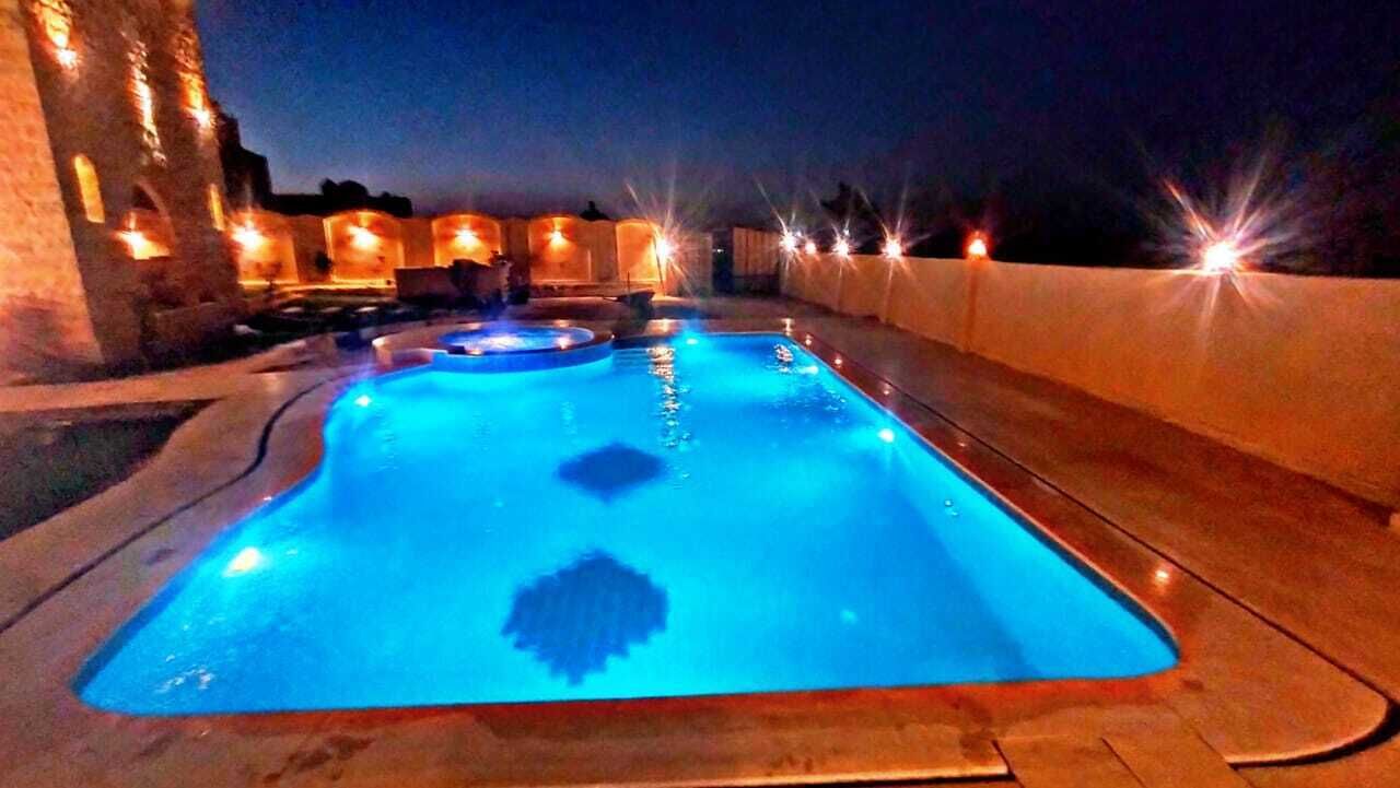 Zwembad met blauwe tint, omringd door een stenen terras en verlicht met sfeerverlichting.
