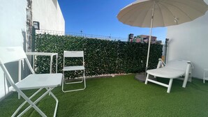 A small outdoor area with artificial grass, a white folding chair, a lounge chair, and a beige umbrella. - The House of Mercedes (La Restinga)