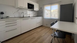 Une cuisine moderne avec des meubles blancs, un four à micro-ondes et une fenêtre qui laisse entrer la lumière naturelle.
