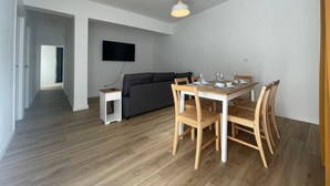 A modern living room with a dining table set for four, a grey sofa, and a flat-screen TV mounted on the wall. - The House of Mercedes (La Restinga)