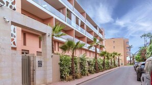 Un immeuble résidentiel à plusieurs étages, doté de balcons, d’une entrée sécurisée et bordé d’une rangée de voitures garées.