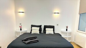 Een moderne slaapkamer met een groot bed, twee nachtkastjes en twee wandlampen.