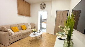 Een woonkamer met een beige bank, een bijzettafeltje en een vaas met bloemen.