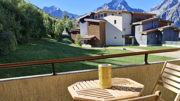 Un balcon avec une table et des chaises, donnant sur un paysage montagneux.