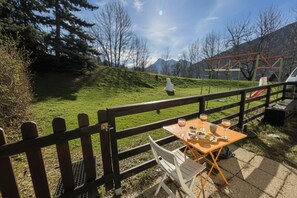 An outdoor dining area with a table and chairs, a wooden fence, and a playground in the background. - Cozy retreat just steps from the slopes (Briançon)