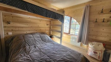 Een houten kamer met een stapelbed, een raam met gordijnen en een ladder.