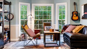 A cozy living room with a leather sofa, a wooden coffee table, and a rocking chair. There is a bookshelf filled with books and decorative items, and a guitar hanging on the wall. - Spacious Family Home in Franklin w/ Playground (Franklin)