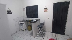 Une petite cuisine équipée d’une cuisinière à gaz, d’un évier et d’une fenêtre. On y trouve deux tabourets et une bouteille de gaz.