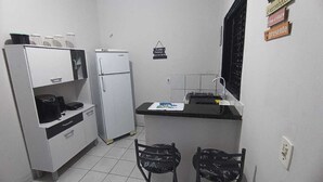 Une cuisine de taille réduite, équipée d’un réfrigérateur, d’un évier et d’un petit plan de travail. On y trouve deux chaises et une table.