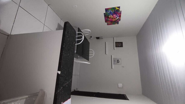 Une petite pièce, de dimensions réduites, avec un sol carrelé, une colonne en marbre noir, un plafond blanc orné d’une œuvre d’art colorée, une petite fenêtre décorée de motifs représentant la lune et le soleil, et un mur blanc avec une petite étagère.