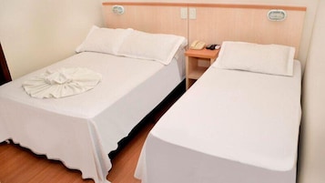 Duas camas de solteiro com lençóis brancos e uma toalha dobrada na cama à esquerda. Um criado-mudo de madeira com um telefone e controle remoto fica entre as camas.