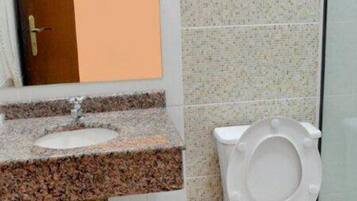 A bathroom with a sink, mirror, toilet, and tiled walls.