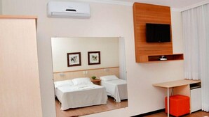 Une chambre d’hôtel avec deux lits, un téléviseur fixé sur un panneau en bois et un petit bureau avec une chaise.