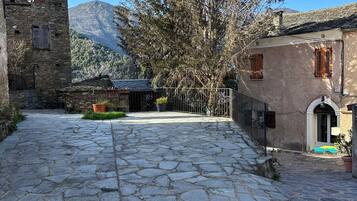 A stone-paved courtyard with a mountain backdrop, stone buildings, and a large tree.