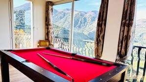 Une table de billard recouverte d’un drap de feutre rouge, placée dans une pièce dotée de grandes fenêtres donnant sur une vue sur les montagnes.