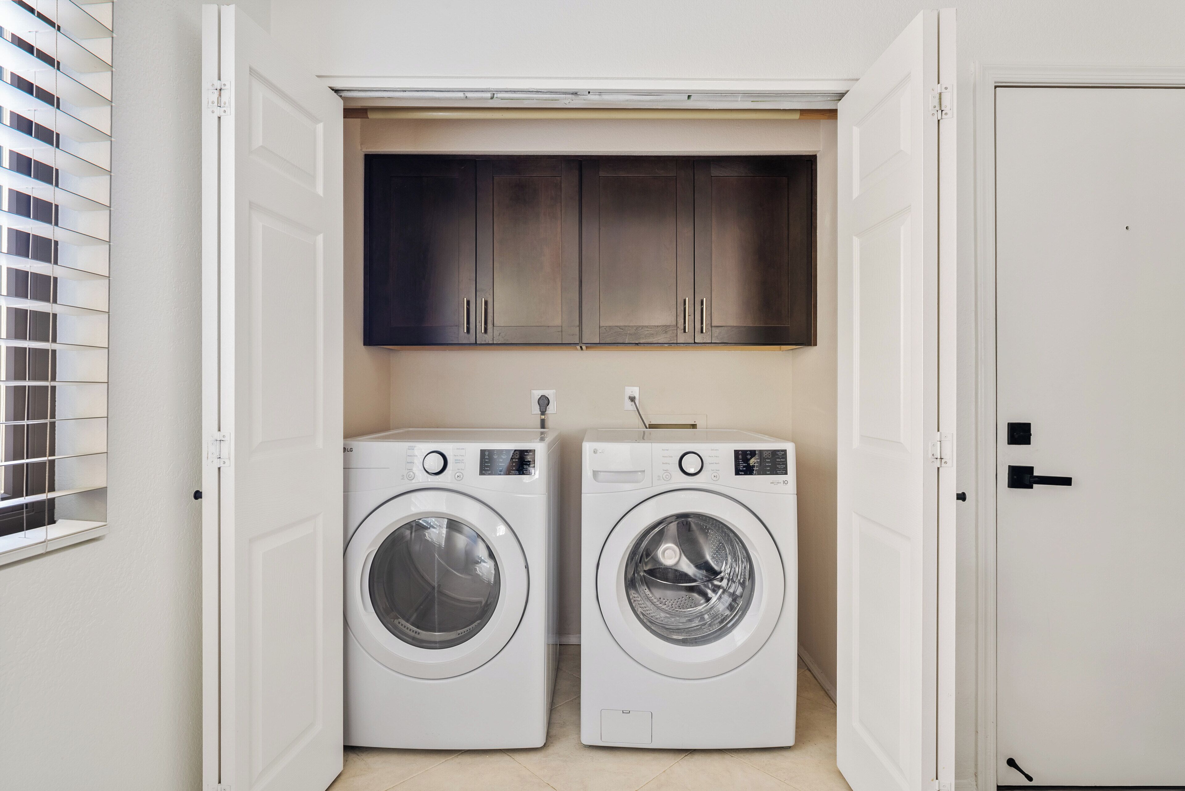 A laundry room with two white front-loading washing machines and a dark wooden cabinet above them.
