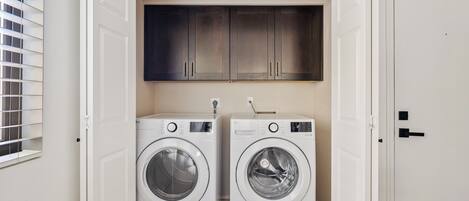 A laundry room with two white front-loading washing machines and a dark wooden cabinet above them.