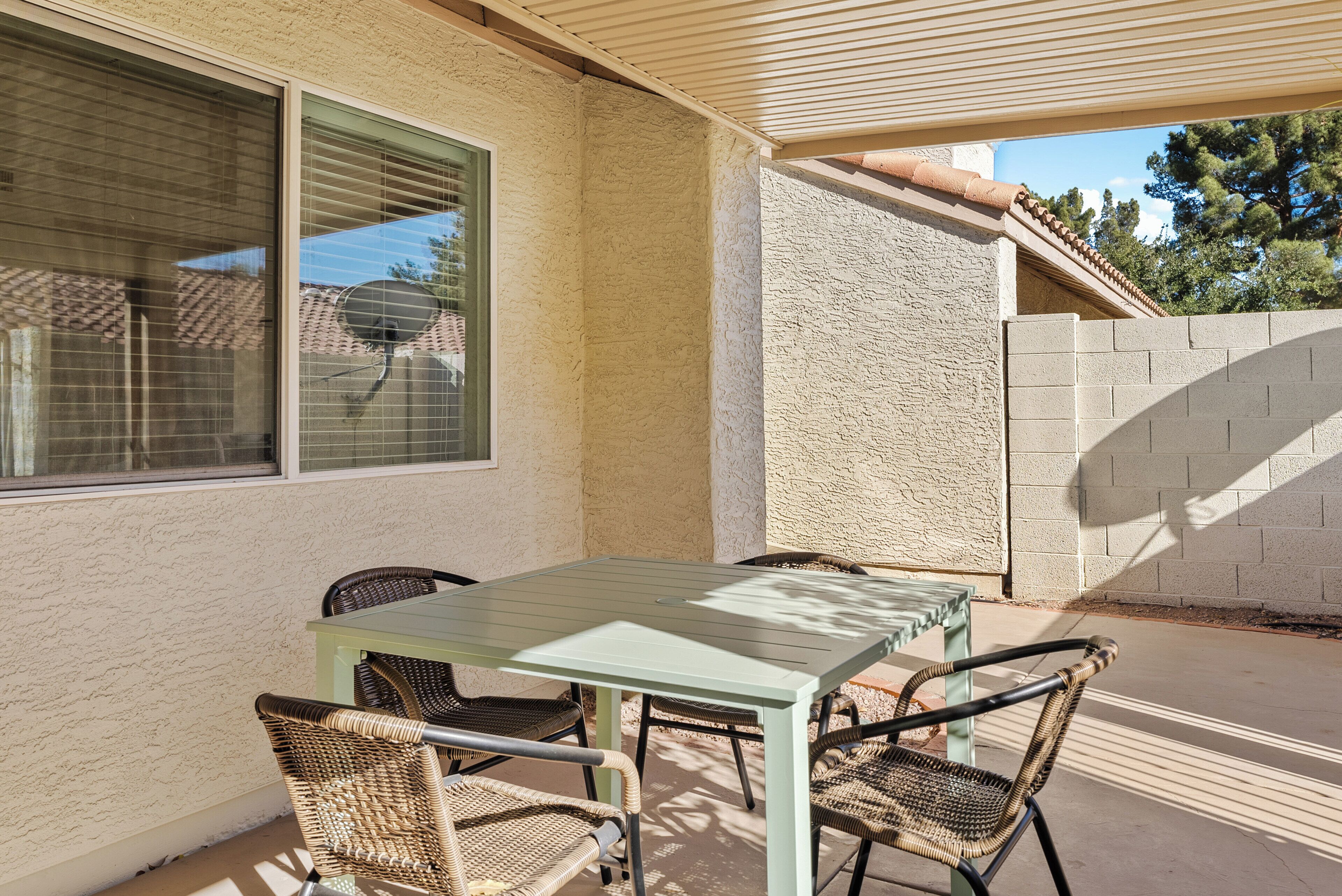 An outdoor patio with a table and chairs, a window, and a textured wall.