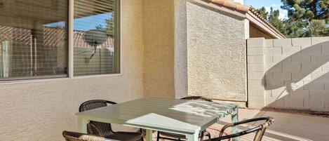 An outdoor patio with a table and chairs, a window, and a textured wall.