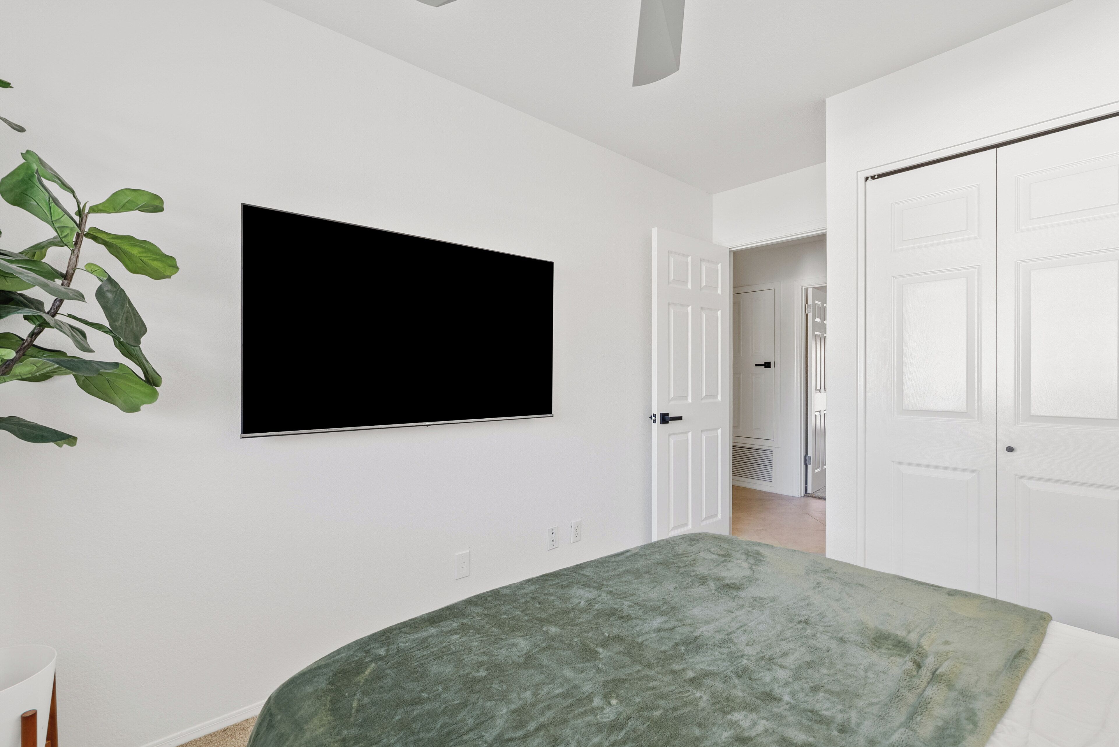 Un dormitorio con una cama, televisión montada en la pared y una puerta que da a otra habitación.