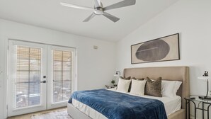 Una camera da letto con un letto, una ventola a soffitto, un quadro incorniciato e una porta con persiane.