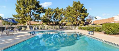 A clear swimming pool with lounge chairs and umbrellas, surrounded by trees and a fence.